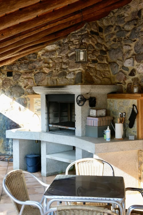 Cocina rústica al aire libre con chimenea de piedra, vigas de madera y comedor en la propiedad rural Balbino, León España