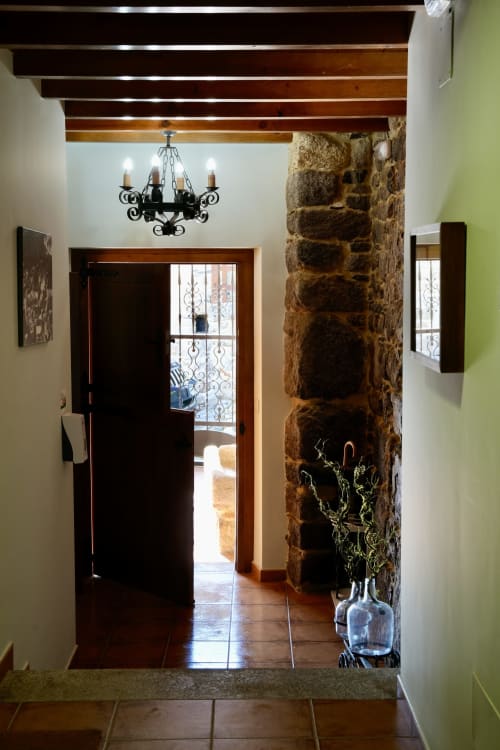 Entrada rústica de piedra con vigas de madera, lámpara de hierro forjado negro y planta decorativa en la propiedad rural de Balbino
