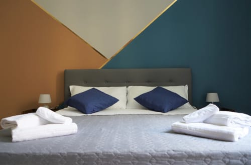 Modern Standard Double Room at Royal Rooms Station Napoli featuring navy pillows, gray headboard, and geometric wall design