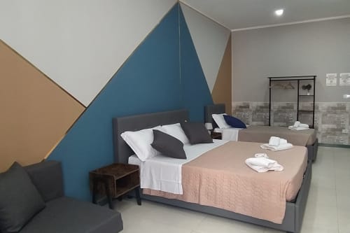Family Room at Royal Rooms Station Napoli with two beds, geometric blue accent wall, and modern furnishings in Naples, Italy