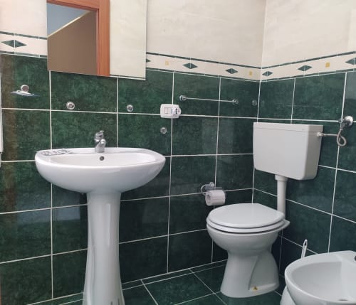 Modern bathroom with pedestal sink, toilet, and green tile walls at Royal Rooms Station Napoli, Naples