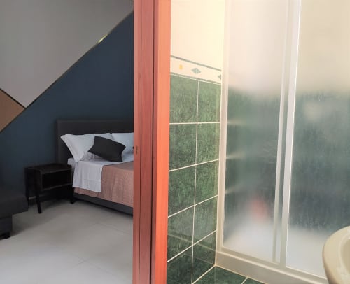 Modern bedroom at Royal Rooms Station Napoli with bed, dark accent wall, large window with city view, and contemporary