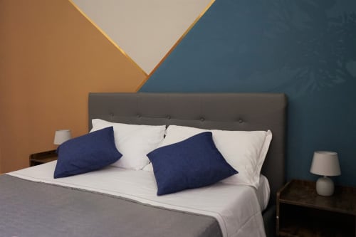 Modern bedroom at Royal Rooms Station Napoli with gray upholstered bed, white linens, navy pillows, and colorful geometric