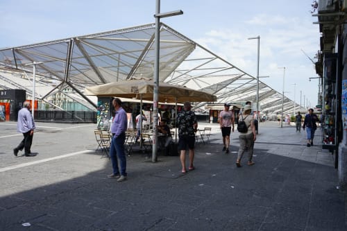 Modern plaza at Royal Rooms Station Napoli with architectural canopy structures and people walking near shops in Naples,