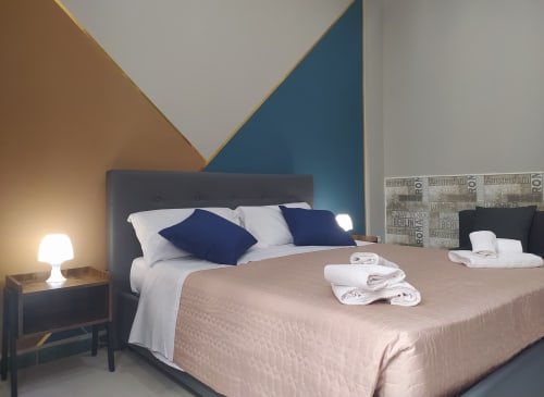 Modern Superior King Room at Royal Rooms Station Napoli with geometric wall design, dark headboard, navy pillows, and city