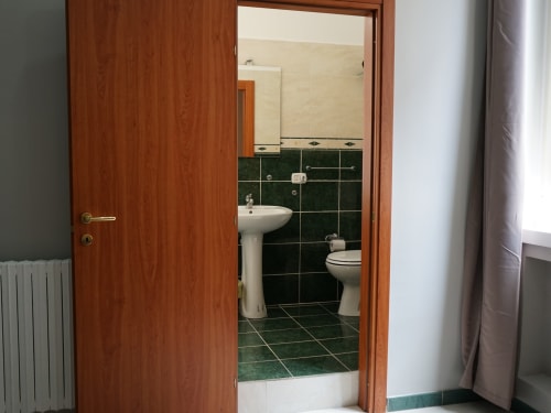 Modern bathroom with green tile flooring, white pedestal sink, and toilet at Royal Rooms Station Napoli in Naples, Italy