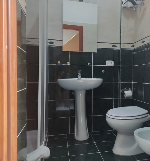 Modern bathroom at Royal Rooms Station Napoli with black tile walls, pedestal sink, toilet, and shower enclosure in Naples,