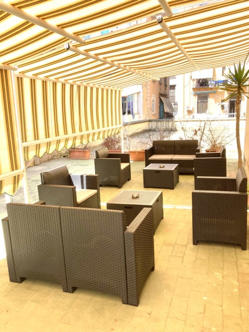 Shaded terrace lounge at Royal Rooms Station Napoli with rattan furniture and striped awning overlooking Naples cityscape