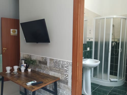 Modern hotel room at Royal Rooms Station Napoli with flat-screen TV, wooden desk, and en-suite bathroom with shower