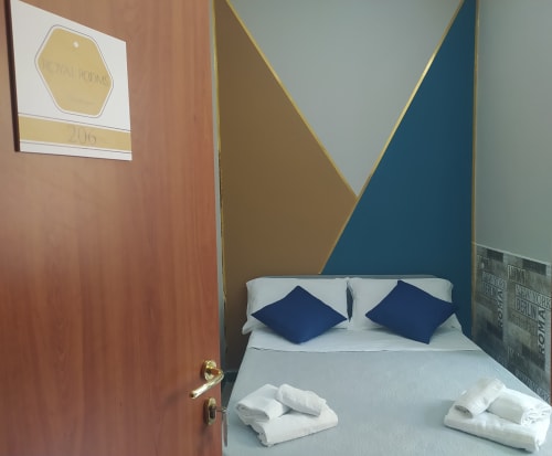 Small double bedroom at Royal Rooms Station Napoli with modern geometric wall art, white bed with navy pillows, and rolled