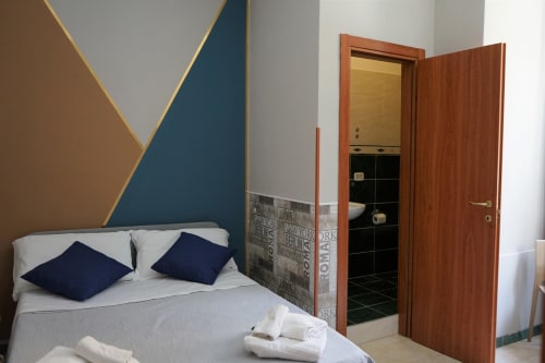 Small double room at Royal Rooms Station Napoli with modern geometric headboard, navy pillows, and en-suite bathroom in