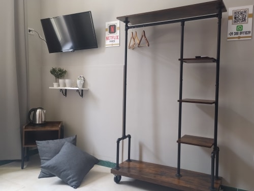 Compact hotel room at Royal Rooms Station Napoli featuring wall-mounted TV, clothing rack, potted plants, kettle, and