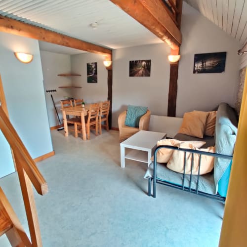 Intérieur cozy du gîte La Ferme De Werpin à Hotton avec poutres en bois, espace détente, table à manger et lit