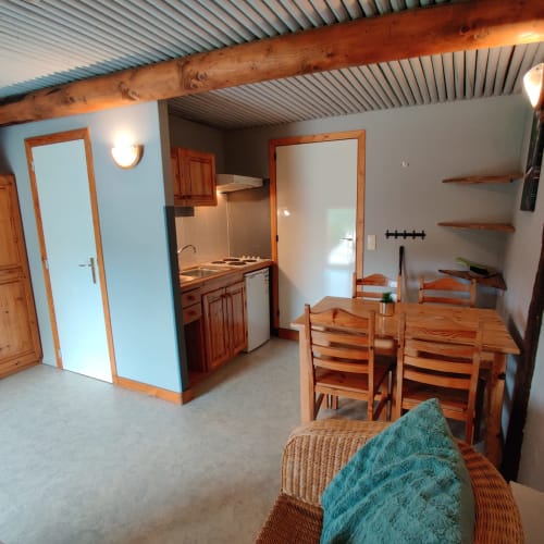 Split-level apartment interior at La Ferme De Werpin with wooden beam ceiling, kitchen area, dining table, and garden views