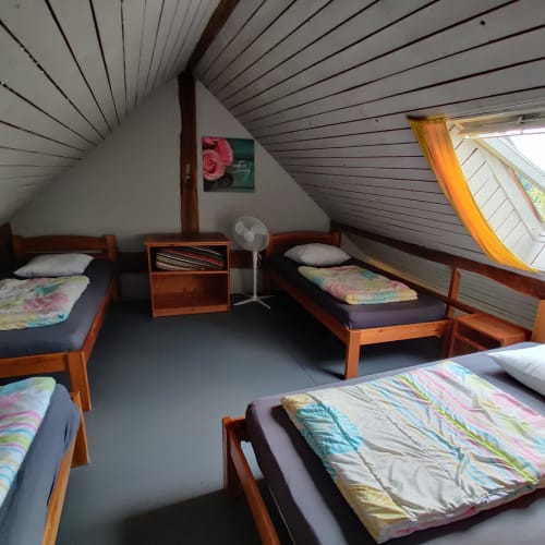 Attic bedroom with four wooden beds, colorful bedding, sloped ceiling, fan, and garden view window at La Ferme De Werpin,