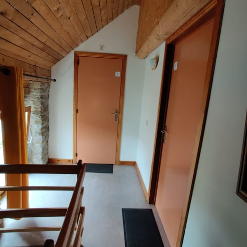 Hallway at La Ferme De Werpin apartment with wooden ceiling beams, orange doors, and black doormats