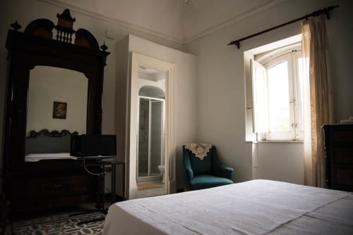 Luminosa camera da letto a B&B Valle Allegra con letto ornato scuro, poltrona turchese e vista sul giardino dalle finestre