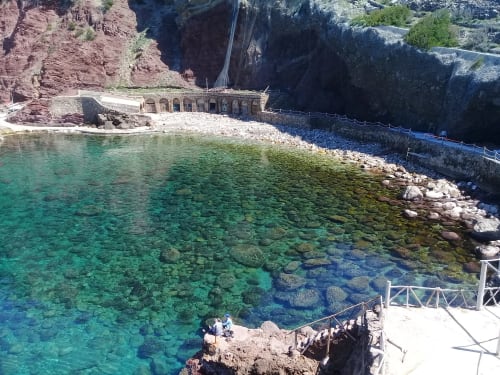 Cala de aguas cristalinas color turquesa con costa rocosa, puente de piedra arqueado y acantilados rojos espectaculares en Petit Hotel Sa Plana