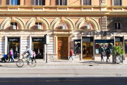 Street view of shops and pedestrians in Rome near Maison Vaticana Guest House, historic building with arched windows