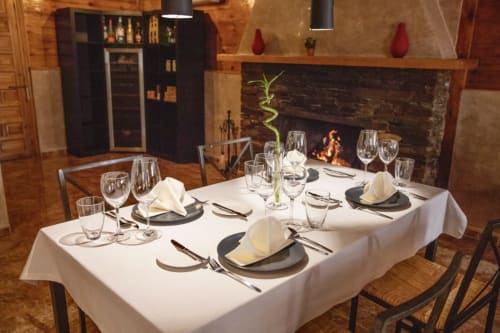 Elegante comedor de El Paraje del Chef en Laroles Nevada con chimenea, mesa servida para cuatro y vigas de madera.