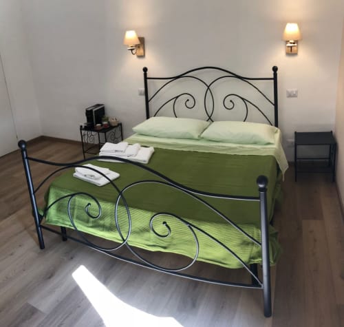 Elegant bedroom at Maison Vaticana Guest House Rome with ornate black iron bed, green bedding, and wall sconces