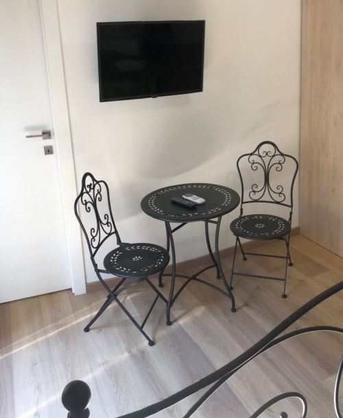Small seating area with wrought iron chairs and table at Maison Vaticana Guest House Rome, wall-mounted TV above