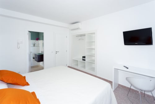 Modern double bedroom at Hotel Sa Roqueta in Can Picafort with white bedding, orange pillows, flat-screen TV, and ensuite
