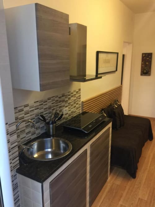Modern kitchenette with black countertop, sink, and wood-grain cabinets at Maison Vaticana Guest House Rome