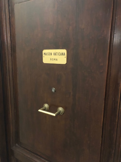 Dark wooden door with brass handle and Maison Vaticana Roma nameplate at guest house in Rome