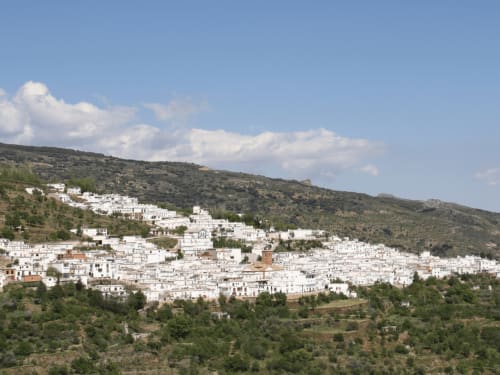 Pueblo blanco de Laroles enclavado en verdes montañas bajo cielo azul, Granada España