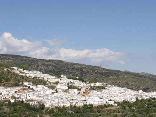 Blanco pueblo andaluz de Laroles acurrucado en las verdes montañas de Sierra Nevada bajo cielo azul