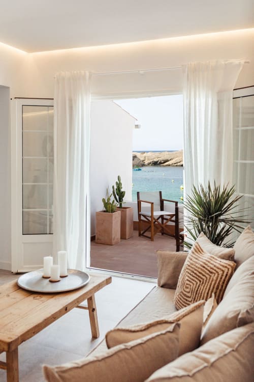 Apartamento moderno en Las Golondrinas con terraza vista al mar, sofá beige, mesa de madera y aguas turquesas del Mediterráneo