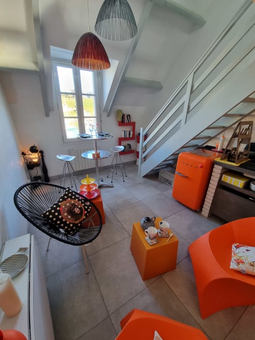 Salon de l'appartement de Carol à Sauzon avec sièges orangés, luminaires suspendus modernes et vue sur la mer à Locmaria, Belle Île