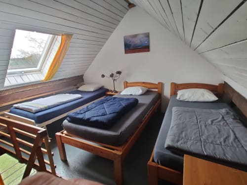 Cozy attic bedroom at La Ferme De Werpin with three wooden beds, skylight window, and garden views in Hotton, Belgium