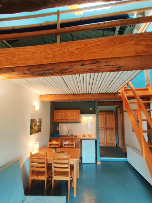 Modern apartment interior at La Ferme De Werpin with wooden beams, dining table, kitchenette, and blue accents in Hotton,