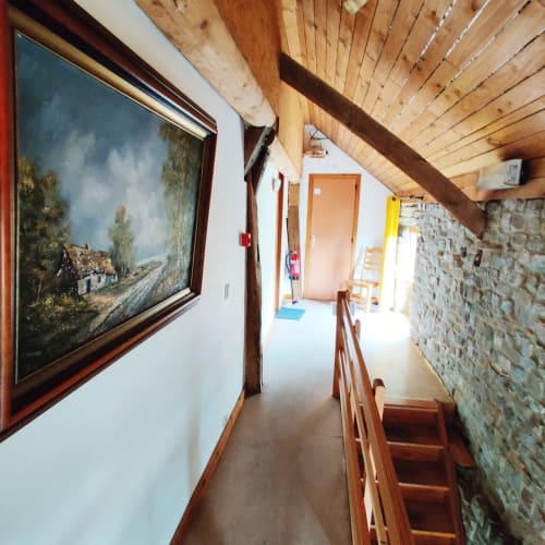 Upstairs hallway at La Ferme De Werpin with wooden beams, stone walls, and framed landscape painting in Hotton, Belgium