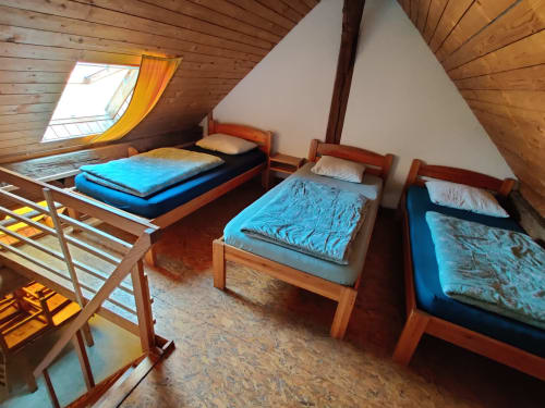 Cozy attic bedroom at La Ferme De Werpin with three wooden beds, blue bedding, sloped wood ceilings, skylight, and cork