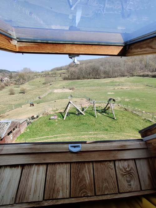 View from La Ferme De Werpin apartment window showing rural garden with play equipment and rolling Belgian countryside