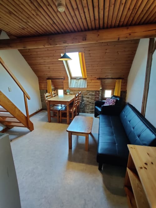 Rustic apartment living room at La Ferme De Werpin with wooden beams, black sofa, dining table, and skylight in Hotton,