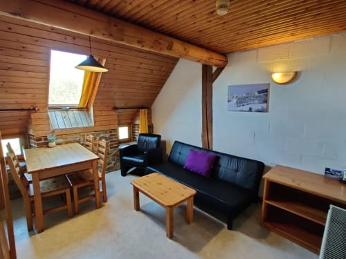 Cozy apartment living room at La Ferme De Werpin with wooden beams, black sofa, dining table, and garden views in Hotton