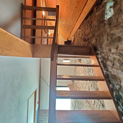 Wooden staircase in La Ferme De Werpin apartment, Hotton, with exposed stone wall and wooden ceiling