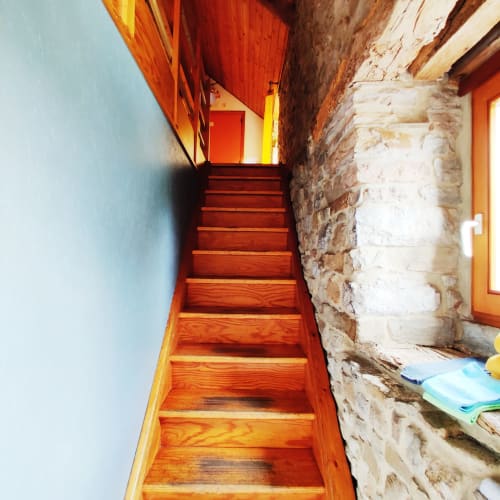 Escalier en bois aux marches rouge-orange montant entre un mur bleu clair et une façade en pierre rustique à La Ferme De Werpin