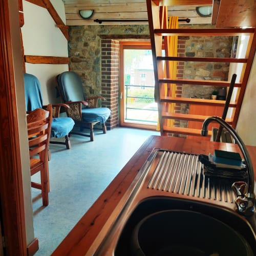Cozy apartment kitchenette with sink, wooden shelving, and seating area at La Ferme De Werpin B&B in Hotton