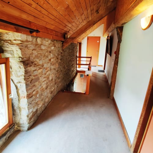 Rustic stone corridor at La Ferme De Werpin with wooden beams, orange doors, and clean white flooring