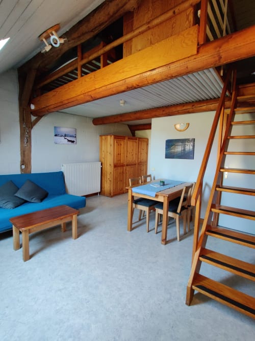 Studio moderne à La Ferme De Werpin à Hotton : poutres apparentes, canapé bleu, coin repas et chambre mezzanine