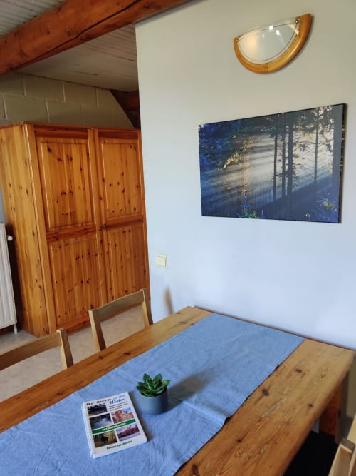 Salle à manger lumineuse avec table en bois, chemin de table bleu, plante en pot et vue forêt à La Ferme De Werpin