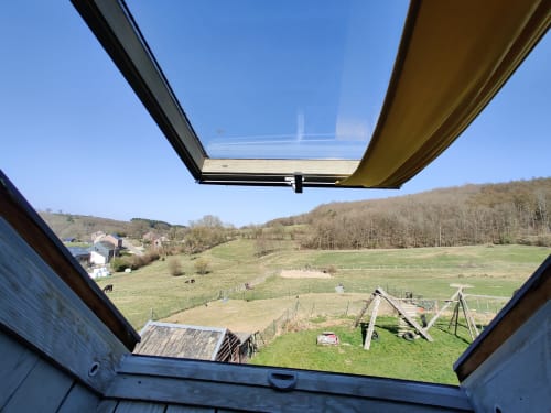 Vue panoramique sous lucarne de la campagne pastorale belge à La Ferme De Werpin, avec champs verdoyants et collines boisées
