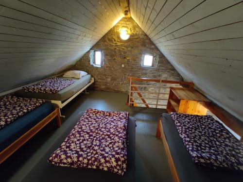 Chambre mansardée à La Ferme De Werpin avec quatre lits simples, murs en pierre et plafond bois incliné à Hotton, Belgique