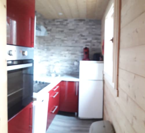 Cuisine moderne du Chalet Cocody à Jausiers avec armoires rouges et blanches, appareils en acier inoxydable et mur en pierre