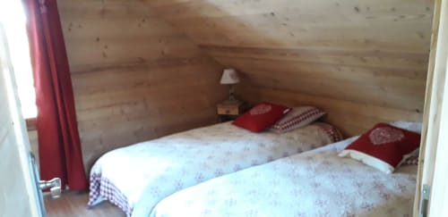 Chambre chaleureuse de la villa Chalets Cocody à Jausiers avec deux lits aux motifs floraux bleus, oreillers rouges et murs en bois